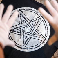 Das Bild zeigt einen fünfzackigen schwarz-weißen Stern auf einem schwarzen Stück Stoff, darüber zwei Hände in weißen Handschuhen.