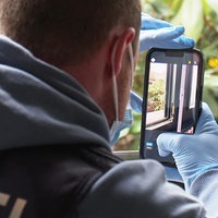 Ermittler Julius Mergelkamp fotografiert mit einem Handy die Schäden an einem Holzfensterrahmen mit Einbruchsspuren