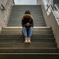 Eine Jugendliche sitzt mit gesenktem Kopf auf einer Treppe, sie trägt eine Kaputze.