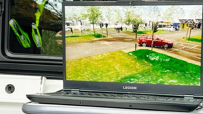 Auf einem Laptop sind eine Kreuzung und ein rotes Auto zu sehen.