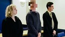 Eine Frau und zwei Männer stehen vor einem Tisch, die Frau steht links, in der Mitte der Verdächtige mit gepixeltem Gesicht, rechts daneben der andere Mann, sie tragen alle dunkle Kleidung