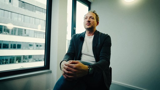 Kriminalhauptkommissar Torben Konrad sitzt in einem leeren Büro vor einer weißen Wand im Büro