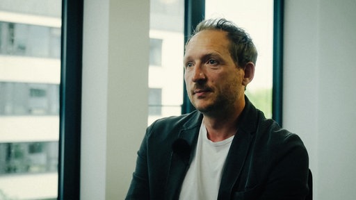 Kriminalhauptkommissar Torben Konrad sitzt in einem leeren Büro vor einer weißen Wand im Büro