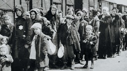 Eine Gruppe von Menschen steht vor einem Viehwaggon. Das Foto ist schwarz-weiß.
