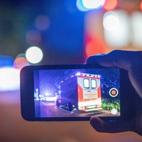 Jemand filmt mit einem Handy einen Krankenwagen mit Blaulicht