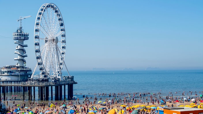Am Strand in Scheveningen liegen viele Menschen, im Hintergrund das Riesenrad