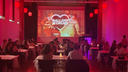 Personen sitzen an Tischen vor einer Leinwand mit der Aufschrift "GALLERY CRUSH"