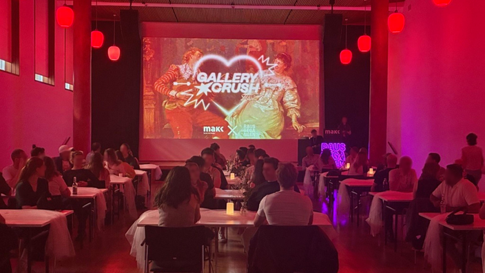 Personen sitzen an Tischen vor einer Leinwand mit der Aufschrift "GALLERY CRUSH"