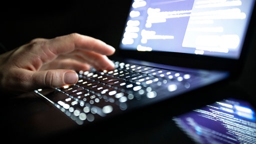 Eine Person tippt mit den Fingern auf einer beleuchteten Laptop-Tastatur