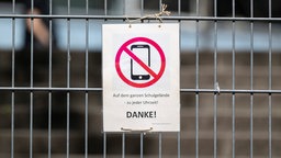 Ein Schild mit einem durchgestrichenen Smartphone und der Aufschrift «Auf dem ganzen Schulgelände - zu jeder Uhrzeit! DANKE!» hängt am Zugangstor zum Schulhof einer Schule