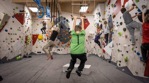 Kinder in der Kletterhalle schwingen an der Sprossenleiter und bouldern in der Wand
