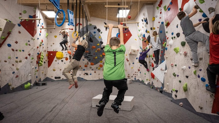 Kinder in der Kletterhalle schwingen an der Sprossenleiter und bouldern in der Wand