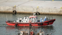 Menschen in Schutzanzügen fahren mit einem Boot zum Kreuzfahrtschiff "Hondius"