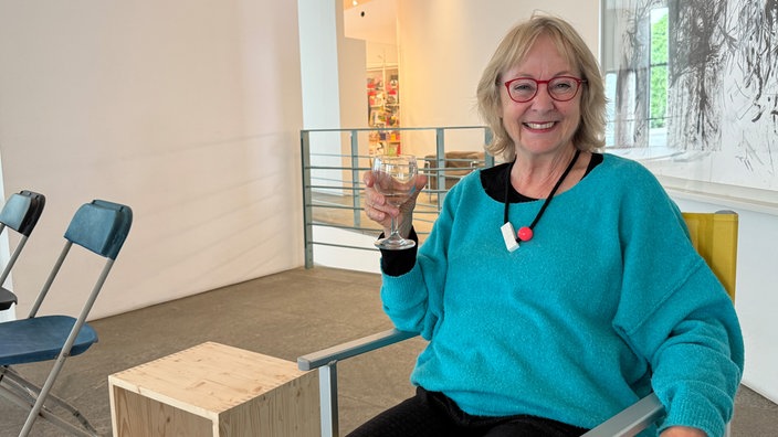 Renate Fröhlig-Striesow sitzt in ihrem gelben Klappstuhl und hält ein Glas in der Hand.