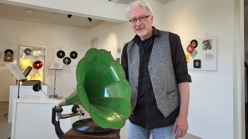 Ein älterer Herr steht neben einem grünen Grammophon