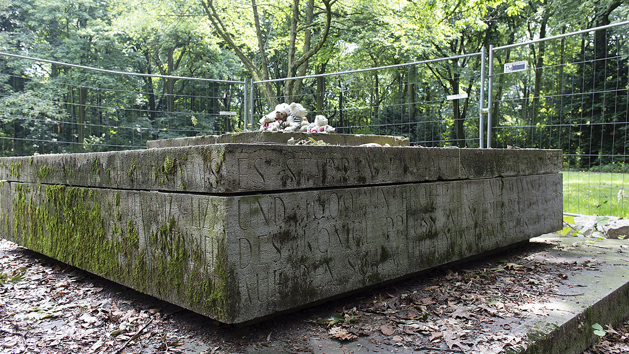 Eingezäunter Sockel eines zerstörten Kriegsdenkmals mit Plüsch-Tieren