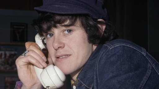 Donovan blickt in die Kamera mit einem Telefonhörer in der Hand