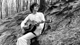 Sänger Donovan mit Gitarre im Wald