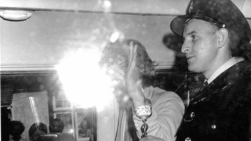 Mick Jagger winkt mit Handschellen aus einem Polizeifahrzeug den Fotografen zu
