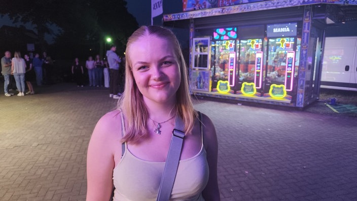 Eine junge Dame steht auf einem Festgelände vor einigen Automaten