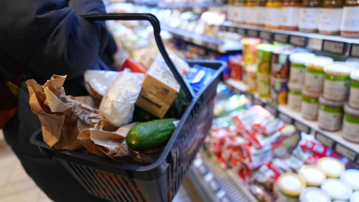 Eine Person trägt einen gefüllten Einkaufskorb durch einen Supermarkt