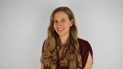 Mirjam Ratmann steht vor einer weißen Wand und schaut in die Kamera