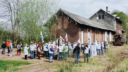 Ein alter Bahnhof. Viele Renter stehen davor. Sie tragen weiße Westen und weiße Flaggen bei sich.
