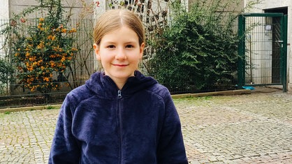 Ein Mädchen in dunkler Jacke mit braunen Haaren lächelt in die Kamera