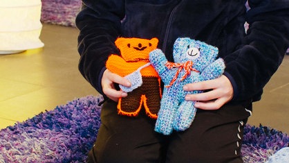Ein Mädchen hält einen orangen und einen blauen Teddybären in der Hand