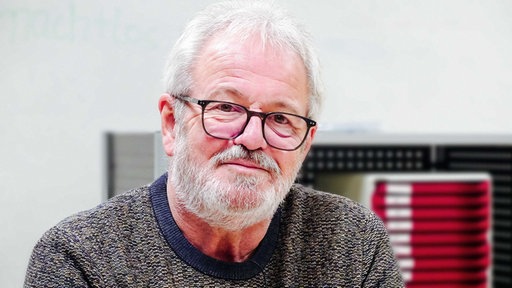 Günter Döker sitzt leicht lächelnd in einem Klassenzimmer