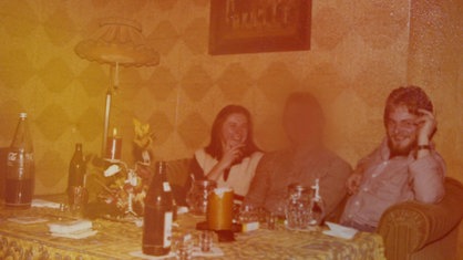 Auf einem alten Foto sitzen Döker und zwei weitere Personen auf einem Sofa, auf dem Tisch vor ihnen stehen Bierflaschen, sowie Bier- und Schnapsgläser