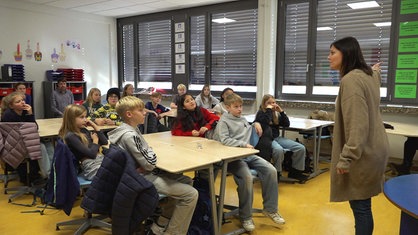 Schauspielerin Stefanie Schäfer präsentiert in einem Klassenraum das Theaterstück "Machtlos", Schülerinnen und Schüler einer sechsten Klasse gucken zu
