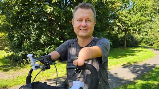 Luwig Lübbers steht in einem Park neben seinem Spazialfahrrad, mit dem er trotz seiner fehlenden Hände fahren kann.