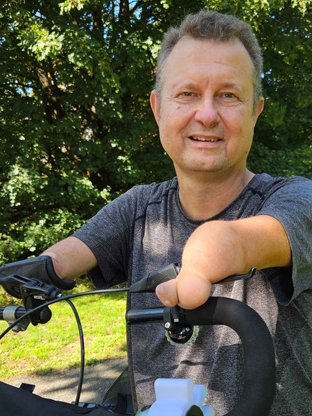 Luwig Lübbers steht in einem Park neben seinem Spazialfahrrad, mit dem er trotz seiner fehlenden Hände fahren kann.