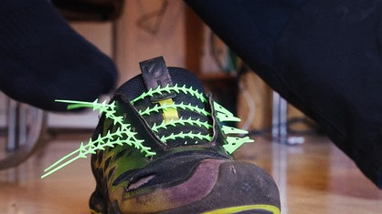 Schwarze Turnschuhe, die statt Schnürsenkeln hellrüne Plastikstifte mit Widerhaken haben.