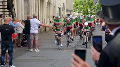 Eine Gruppe Fahrradfahrer in grünen Trikots wird bei der Zieleinfahrt begrüßt