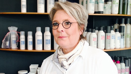Carola Neumann steht in ihrem Friseursalon in Ahlen, im Hintergrund stehen Shampooflaschen in einem Regal