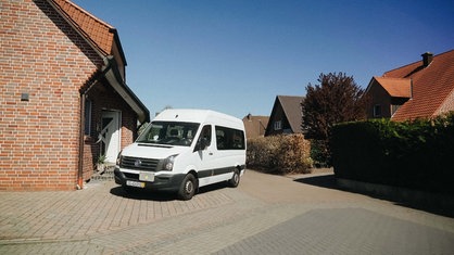 Auf einem Parkplatz vor einem Haus parkt ein weißer Transporter.