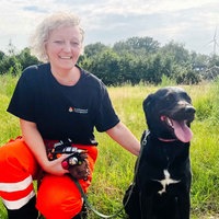 Eine Frau und eine Hündin hocken auf der Wiese.
