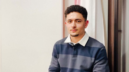 Ein junger Mann blickt in die Kamera, er trägt einen blau gestreiften Pulli