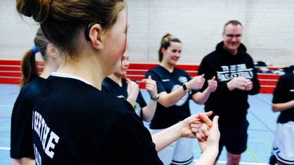 Lilly Schmidt und ihr Team stehen im Kreis und machen Gebärden.