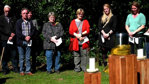 Einige Menschen stehen auf einem Friedhof um eine Urne und gedenken eines Toten