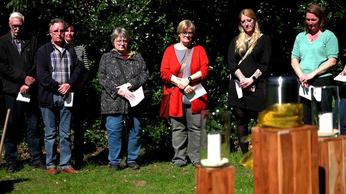 Einige Menschen stehen auf einem Friedhof um eine Urne und gedenken eines Toten