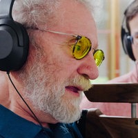Jürgen Klamann beim Schießen. Er trägt eine Brille mit gelben Gläsern. Neben ihm steht sein Trainer, beide haben Kopfhörer auf.