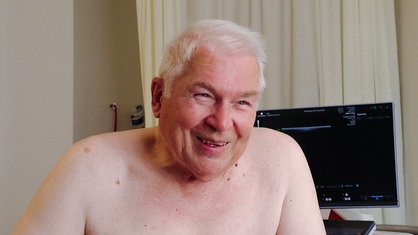 Ernst Sprick sitzt mit freiem Oberkörper auf einer Liege in einem Arztzimmer