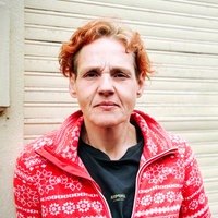 Susan steht in einem rot-weißen Pullover vor einer Wand und guckt in die Kamera