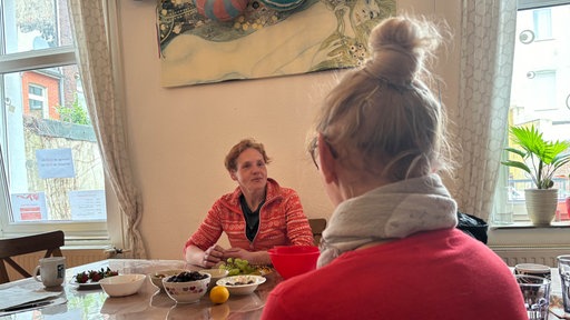 Susan sitzt im Café "Come In" in Dortmund am Esstisch, ihr gegenüber sitzt eine Mitarbeiterin