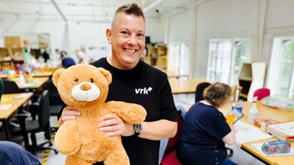 Ein Mann hält einen braunen Teddybär mit dunklen Augen.