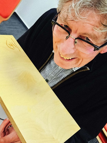 Michael Philipps, graue Haare, schwarze Brille, sitzt vor einem Holzkasten, in dem er über einen Spiegel versucht, kleine Papierkugeln mit Messer und Gabel aufzunehmen.
