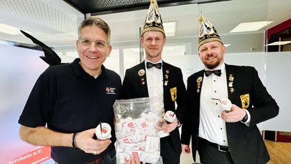 v.l. Michael Hendricks vom DRK Niederrhein und zwei Mitglieder des Karnevalsvereins Alpen-Veen. Sie halten Gläser mit dem Trinkschutz in den Händen.